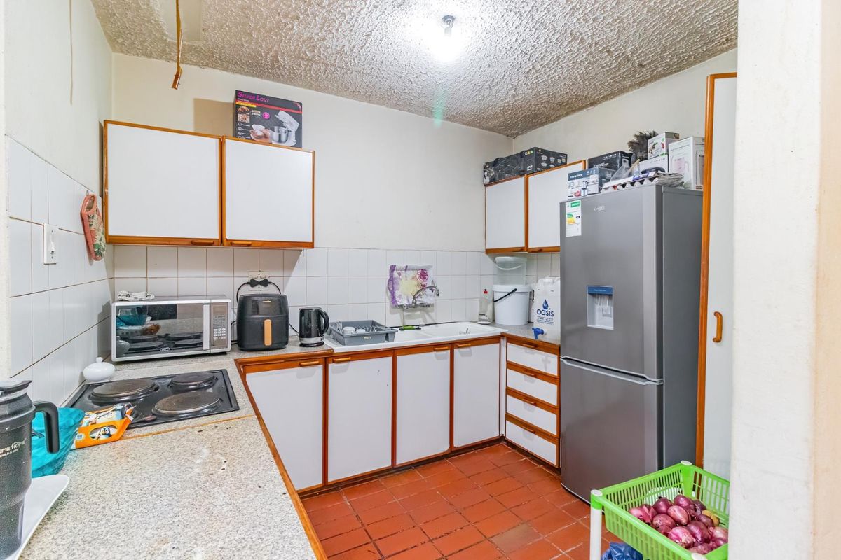 A functional kitchen featuring built-in cabinetry, laminate countertops, an electric hob, and a double basin sink with tiled backsplash and flooring.