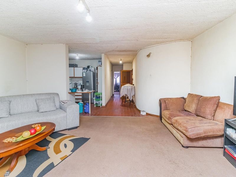Open plan living area featuring a combination of carpeted and tiled flooring with a textured ceiling, connecting to a kitchen and hallway space.