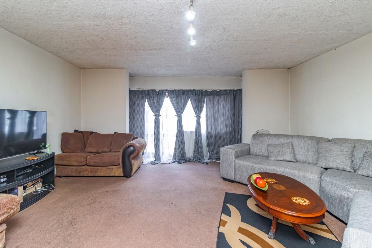A spacious living room featuring textured ceilings and access to a balcony through sliding glass doors, offering a blank canvas for renovation.