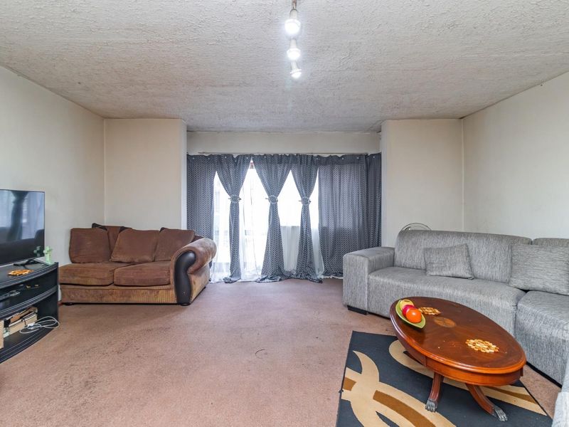 A spacious living room featuring textured ceilings and access to a balcony through sliding glass doors, offering a blank canvas for renovation.