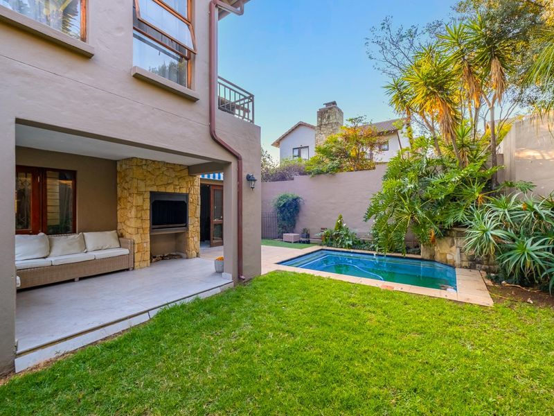 Covered patio area featuring a built-in fireplace with stone cladding, overlooking a private garden with a swimming pool and established landscaping.