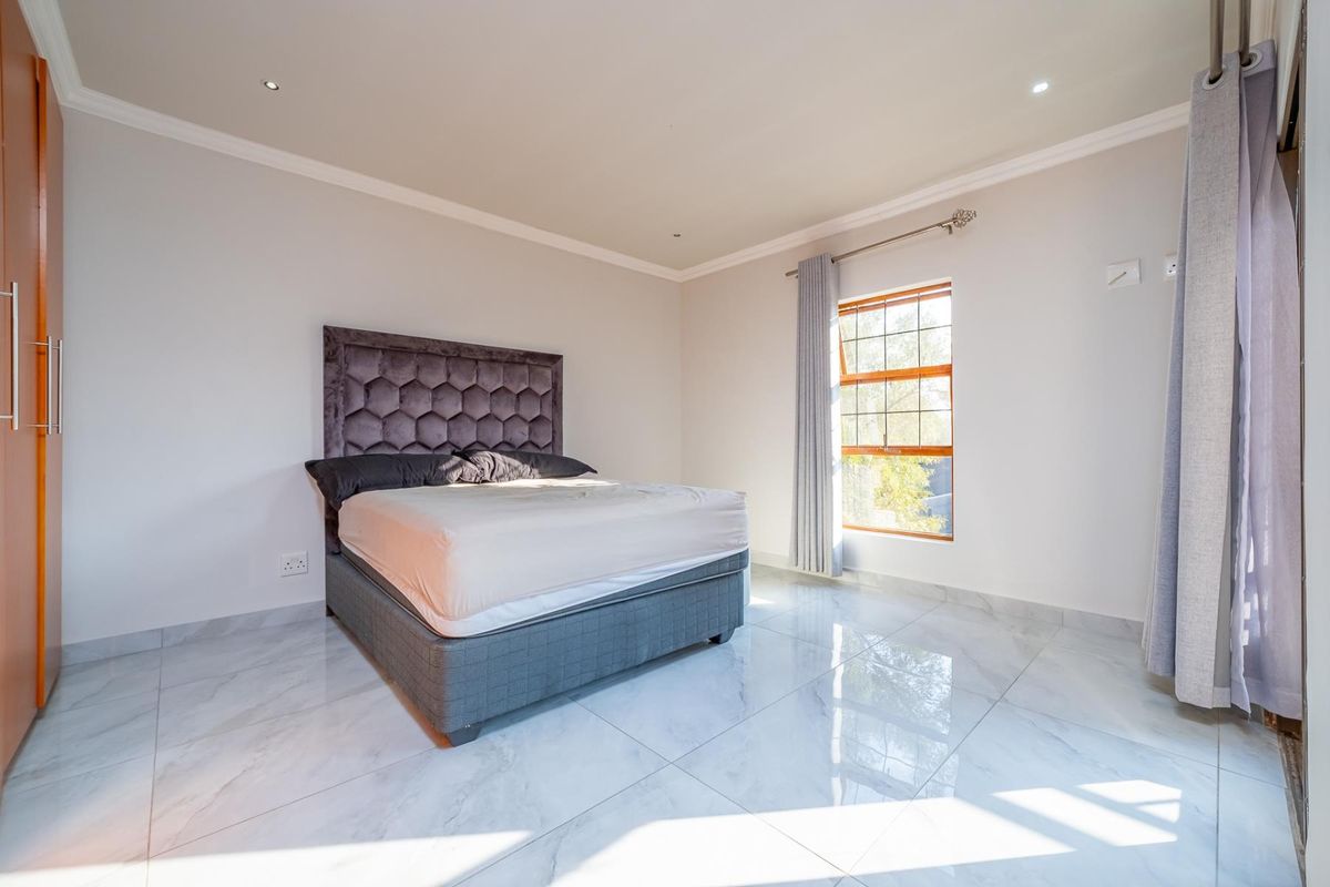 A bright and spacious bedroom featuring polished marble-look tiled flooring, built-in wardrobe storage, and recessed downlighting.