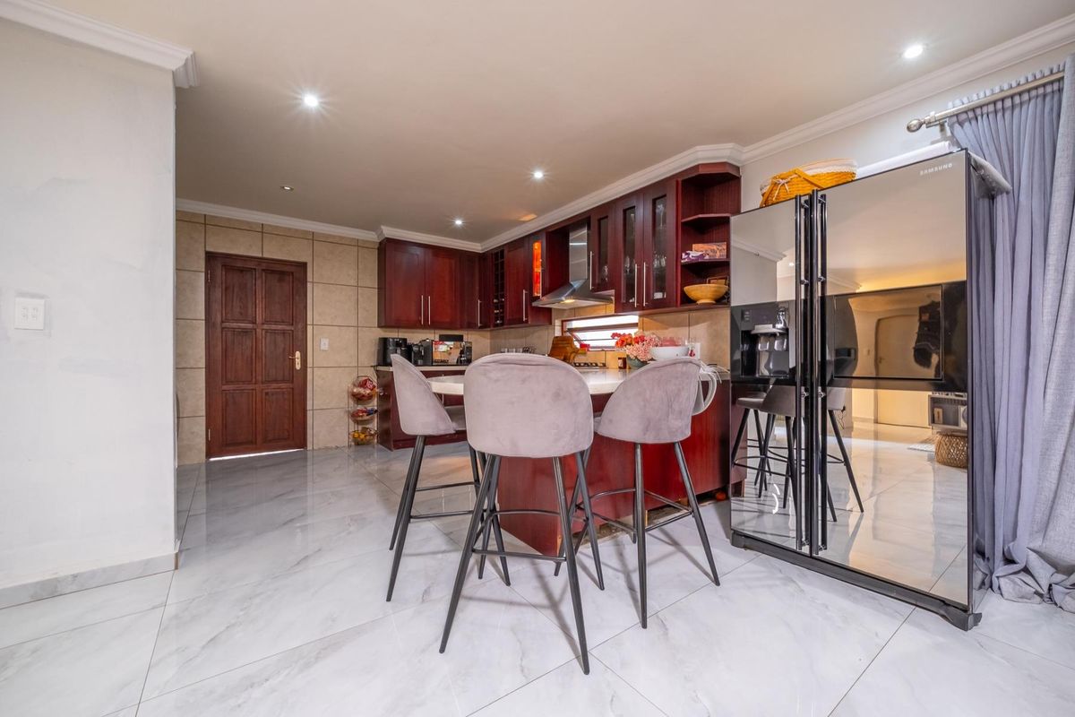 A well-maintained kitchen featuring dark wood cabinetry, stone countertops, a central breakfast island, and modern tiled flooring with recessed lighting.
