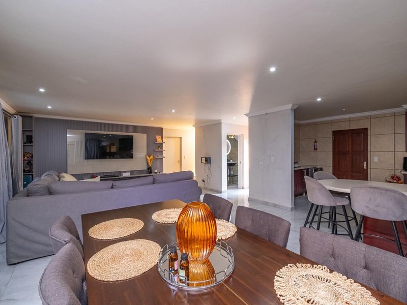 Spacious open-plan living area featuring a dining space, modern kitchen with island, and a dedicated media wall with recessed lighting.