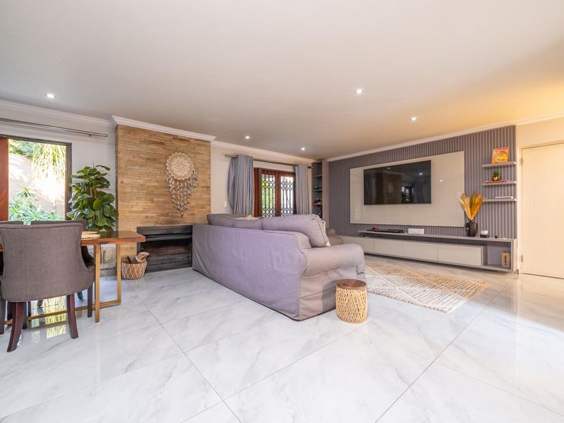 Spacious open-plan living area featuring a stone-clad fireplace, modern built-in media cabinetry, and polished tiled flooring with recessed lighting.