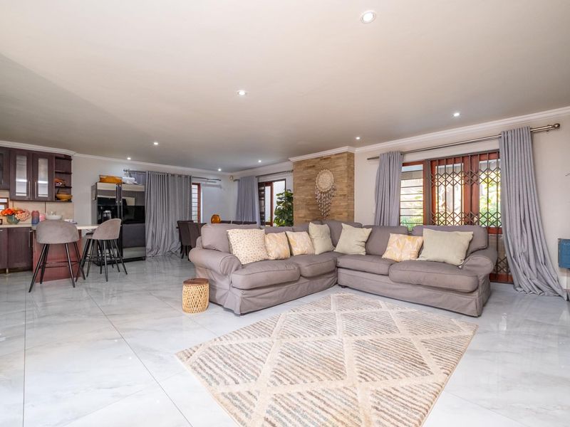 Spacious open-plan living area featuring polished porcelain tiles, a stone feature wall, and a modern kitchen with a breakfast counter.