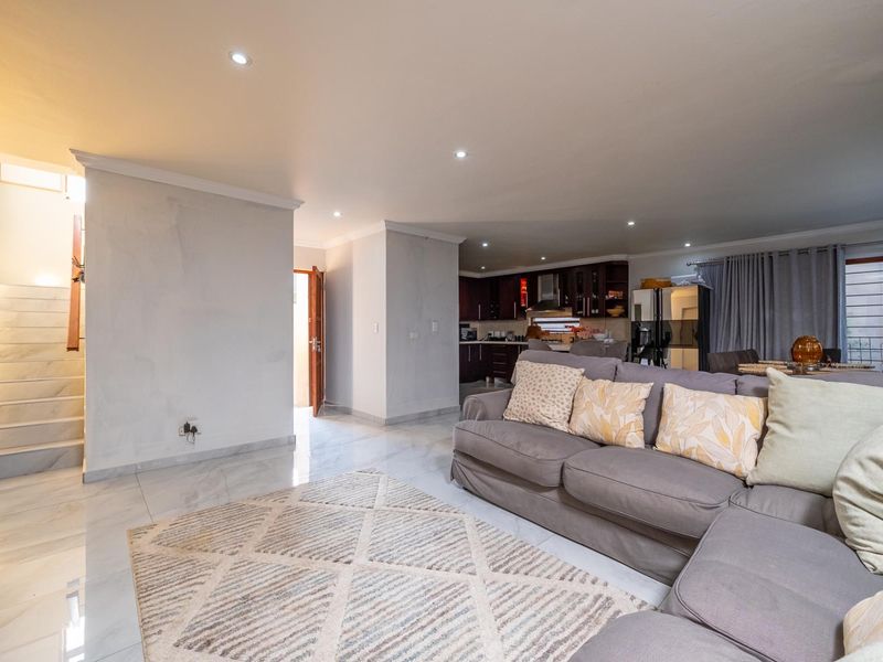 Spacious open-plan living area featuring polished marble-look flooring, recessed lighting, and an integrated kitchen with dark cabinetry, leading to an internal staircase.