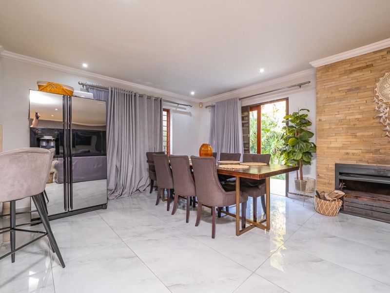 Spacious open-plan dining area featuring a striking stone-clad fireplace, polished marble-look flooring, and direct access to the outdoor garden space.