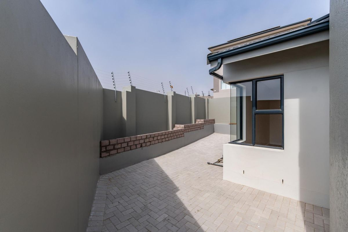 A clean, paved rear courtyard area featuring high boundary walls with integrated electric fencing and modern aluminium window frames.