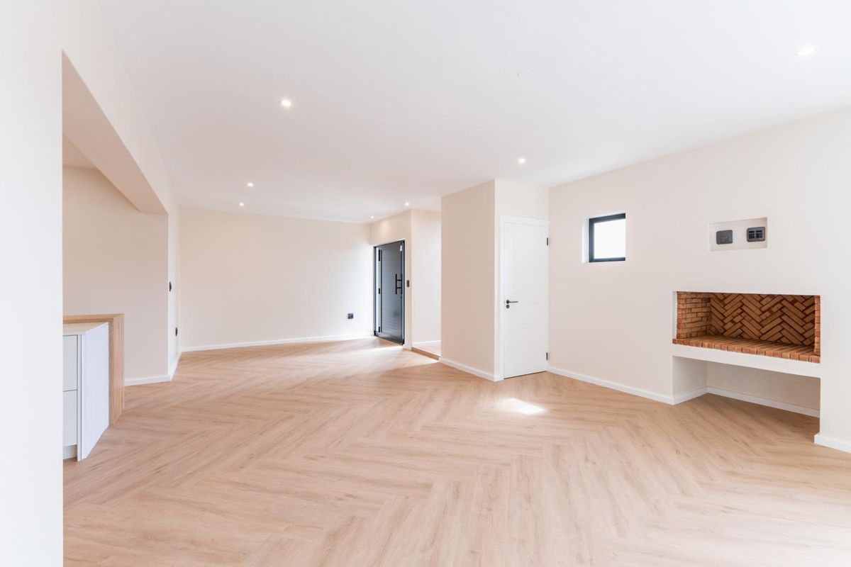 Spacious, light-filled living area featuring modern herringbone flooring, recessed lighting, and a charming built-in brick fireplace.
