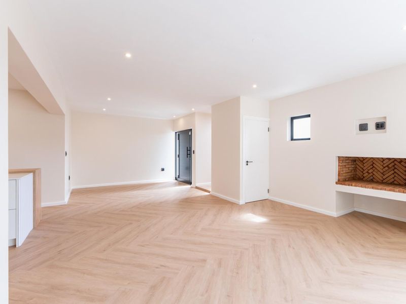 Spacious, light-filled living area featuring modern herringbone flooring, recessed lighting, and a charming built-in brick fireplace.