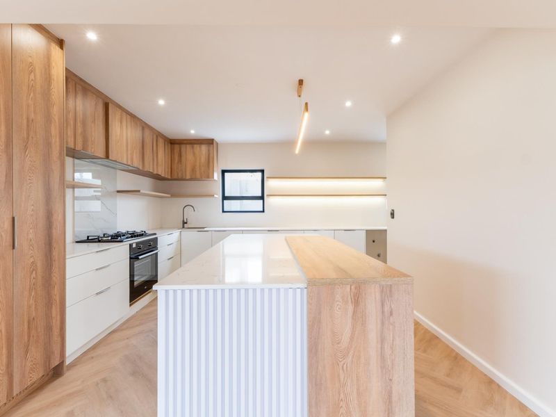 Modern, high-end kitchen featuring a large island with stone countertops, integrated appliances, wood-grain cabinetry, and elegant herringbone flooring.
