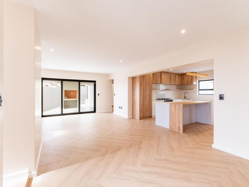 Modern open-plan living area featuring herringbone flooring, recessed lighting, and a contemporary kitchen with a central island, leading to an outdoor patio with braai.