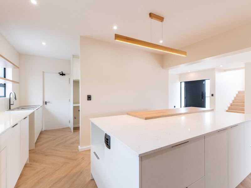 Modern, minimalist kitchen featuring a large central island with quartz countertops, sleek white cabinetry, and elegant herringbone flooring in a bright, open-plan layout.