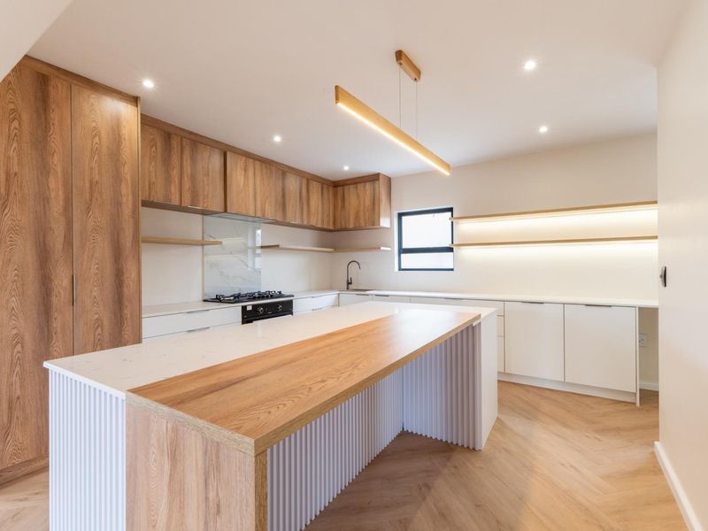 Modern kitchen featuring a large island with wood and white fluted detailing, stone countertops, integrated cabinetry, and herringbone flooring.