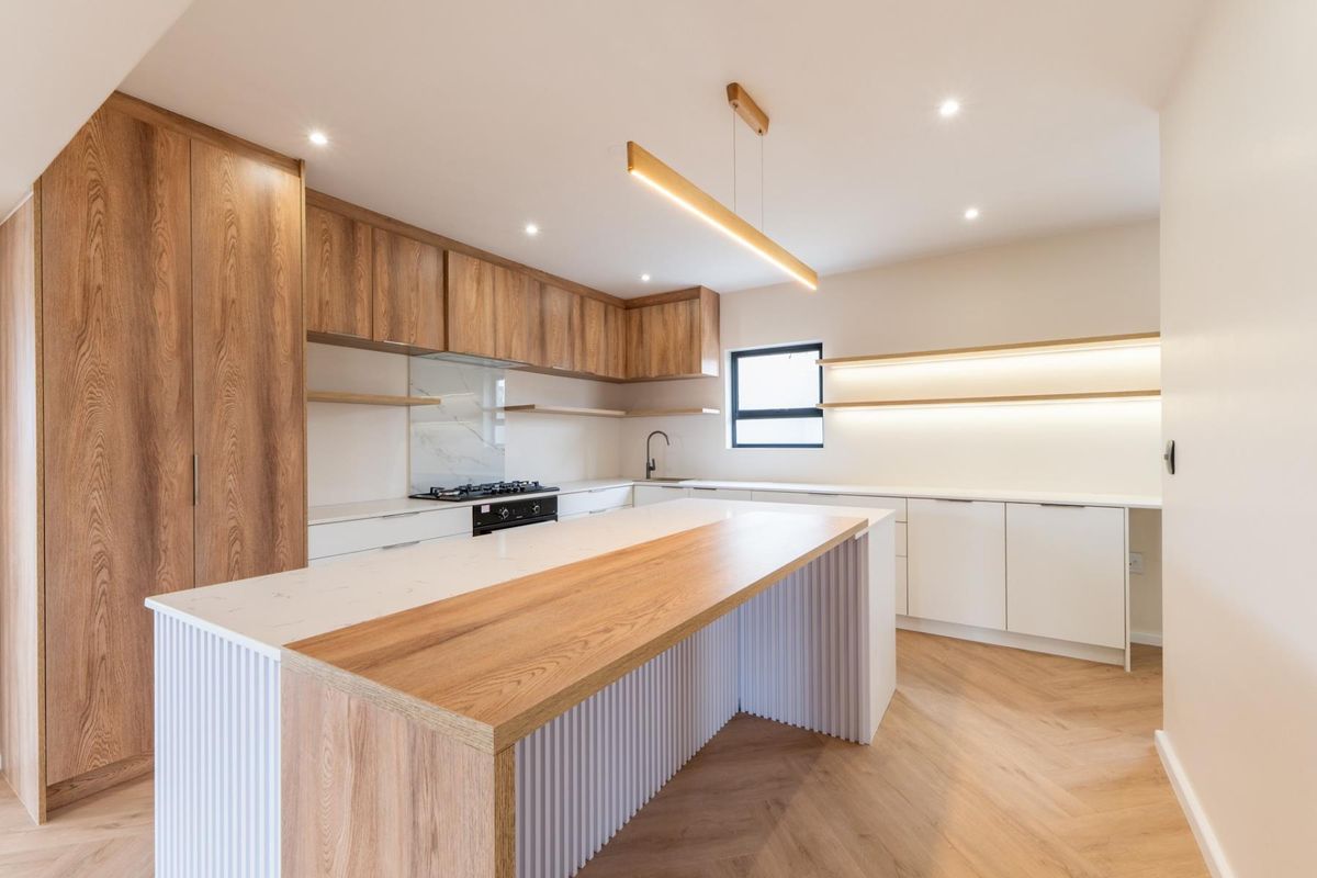 Modern kitchen featuring a large island with wood and white fluted detailing, stone countertops, integrated cabinetry, and herringbone flooring.