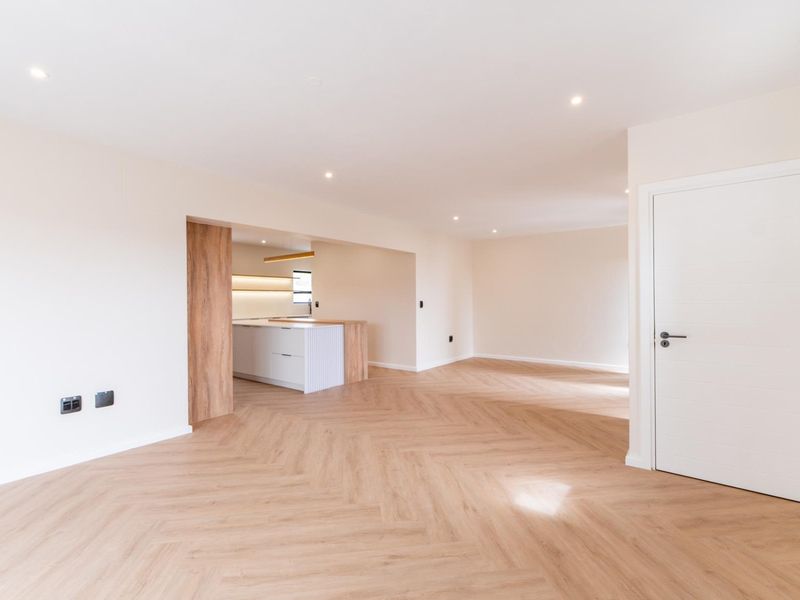Spacious open-plan living area featuring modern herringbone wood flooring, recessed lighting, and a sleek, contemporary kitchen with a central island.
