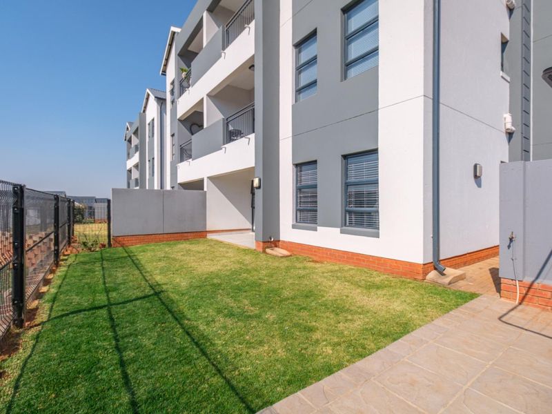 A well-maintained ground floor apartment exterior featuring a private lawn area, paved walkway, and modern building facade with balconies.