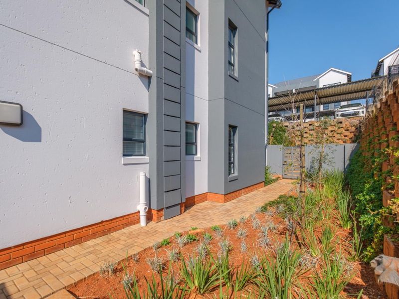 A well-maintained rear exterior view of the apartment building featuring a paved walkway, landscaped garden, and a sturdy retaining wall.