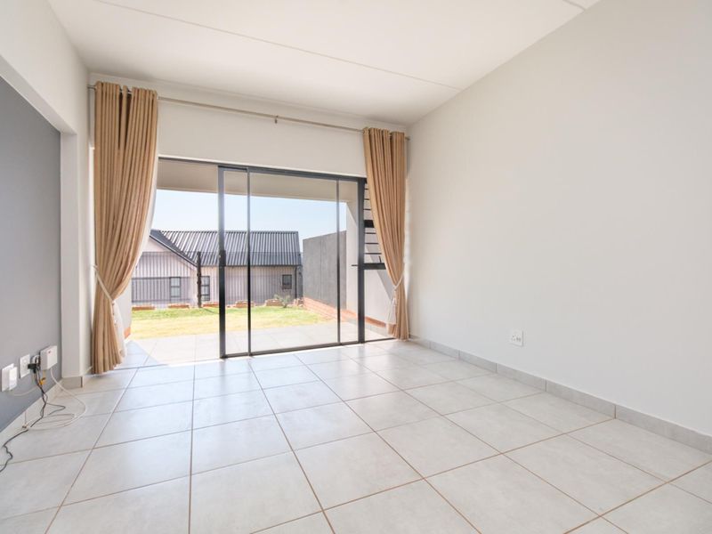 A bright, empty living room featuring neutral ceramic floor tiles and a large sliding glass door providing access to an outdoor patio area.