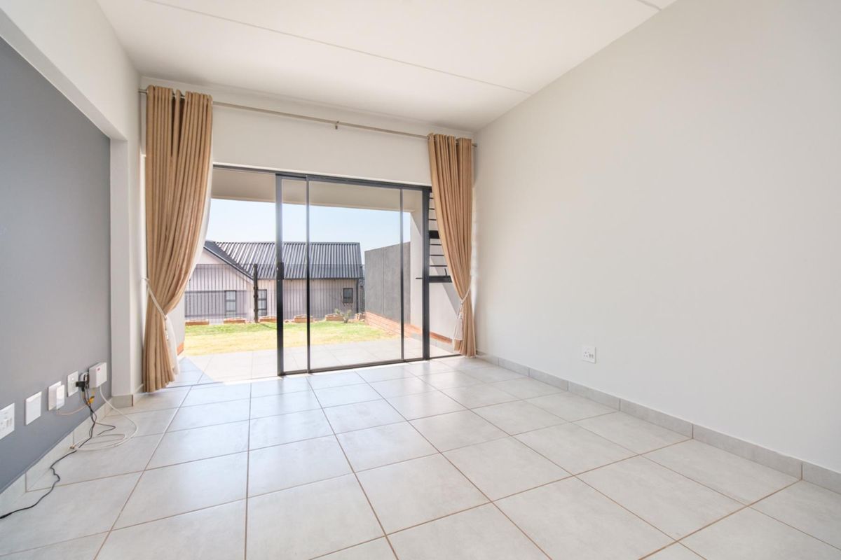 A bright, empty living room featuring neutral ceramic floor tiles and a large sliding glass door providing access to an outdoor patio area.