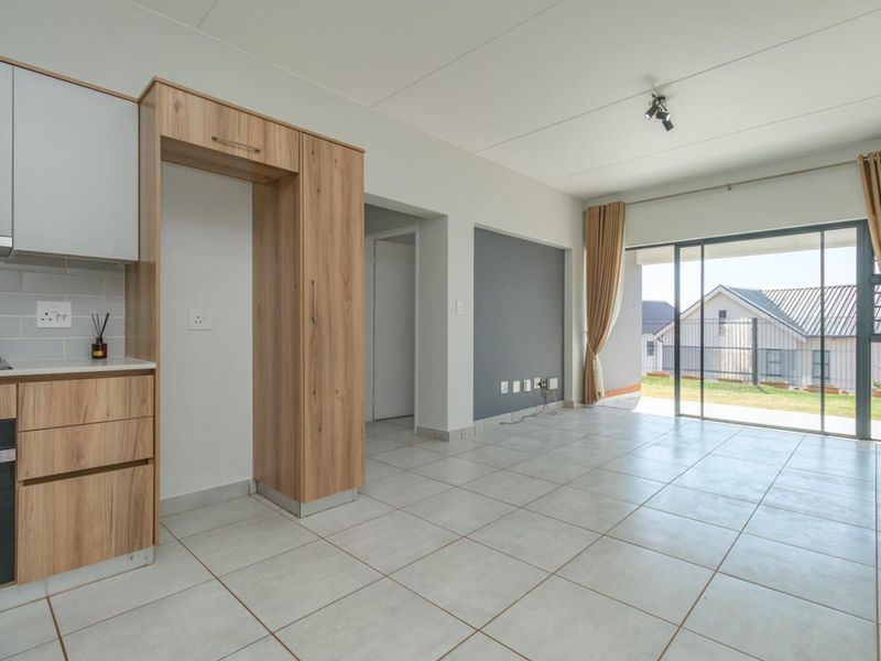 Modern open-plan kitchen and living area featuring tiled floors, sleek wood-finish cabinetry, and large sliding glass doors leading to an outdoor space.