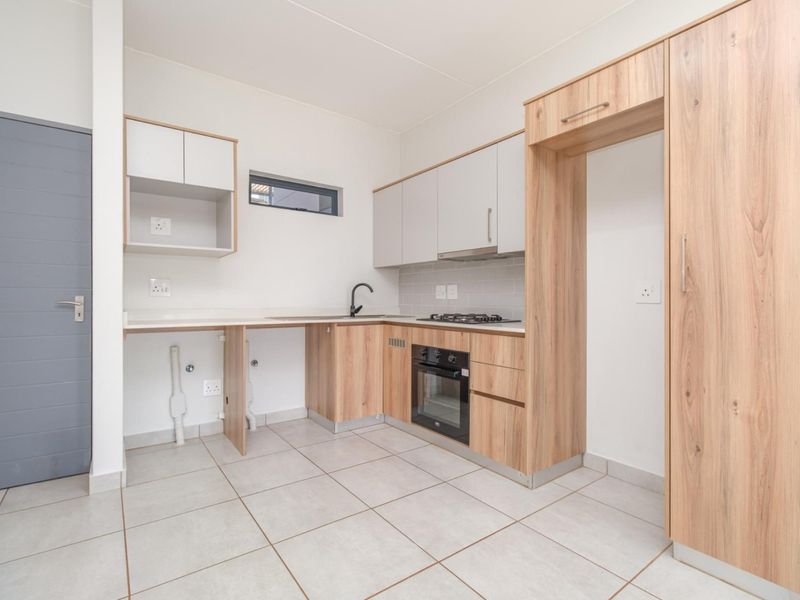 Modern kitchen featuring light wood-tone cabinetry, integrated oven and gas hob, subway tile backsplash, and neutral tiled flooring in an open-plan layout.