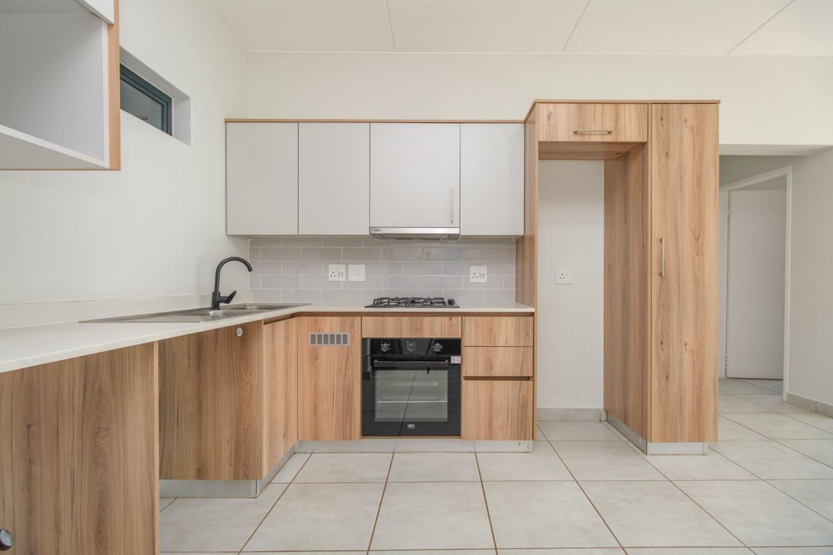 Modern kitchen featuring light wood-look cabinetry, stone-effect countertops, built-in oven, gas hob, extractor fan, and neutral tiled flooring.