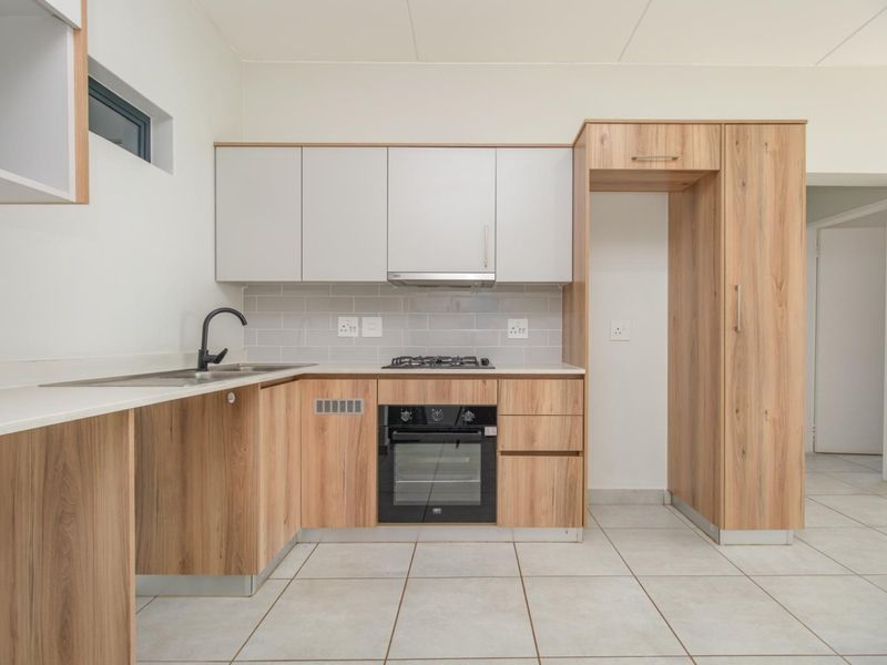 Modern kitchen featuring light wood-look cabinetry, stone-effect countertops, built-in oven, gas hob, extractor fan, and neutral tiled flooring.