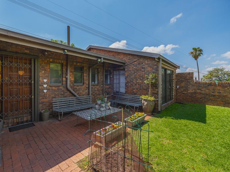 A private rear courtyard featuring brick paving, a well-maintained lawn, and a secure entrance with a metal security gate.