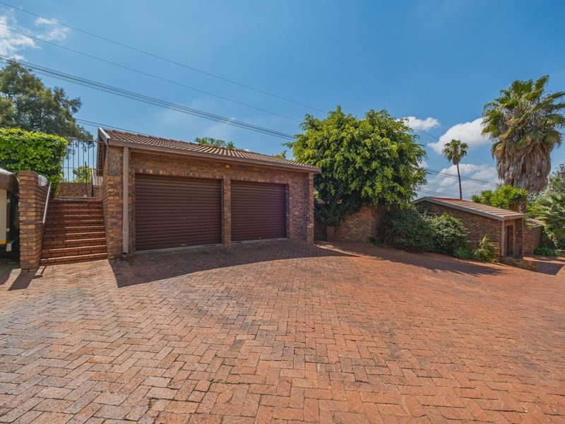 A double garage with roller doors and a brick-paved driveway, featuring an adjacent brick staircase leading to an elevated area.