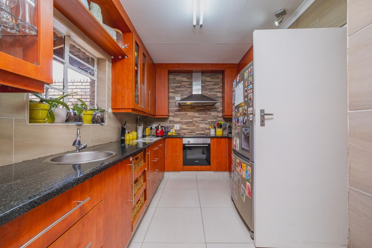 A functional galley-style kitchen featuring warm-toned wooden cabinetry, granite countertops, a tiled backsplash, and integrated stainless steel appliances.