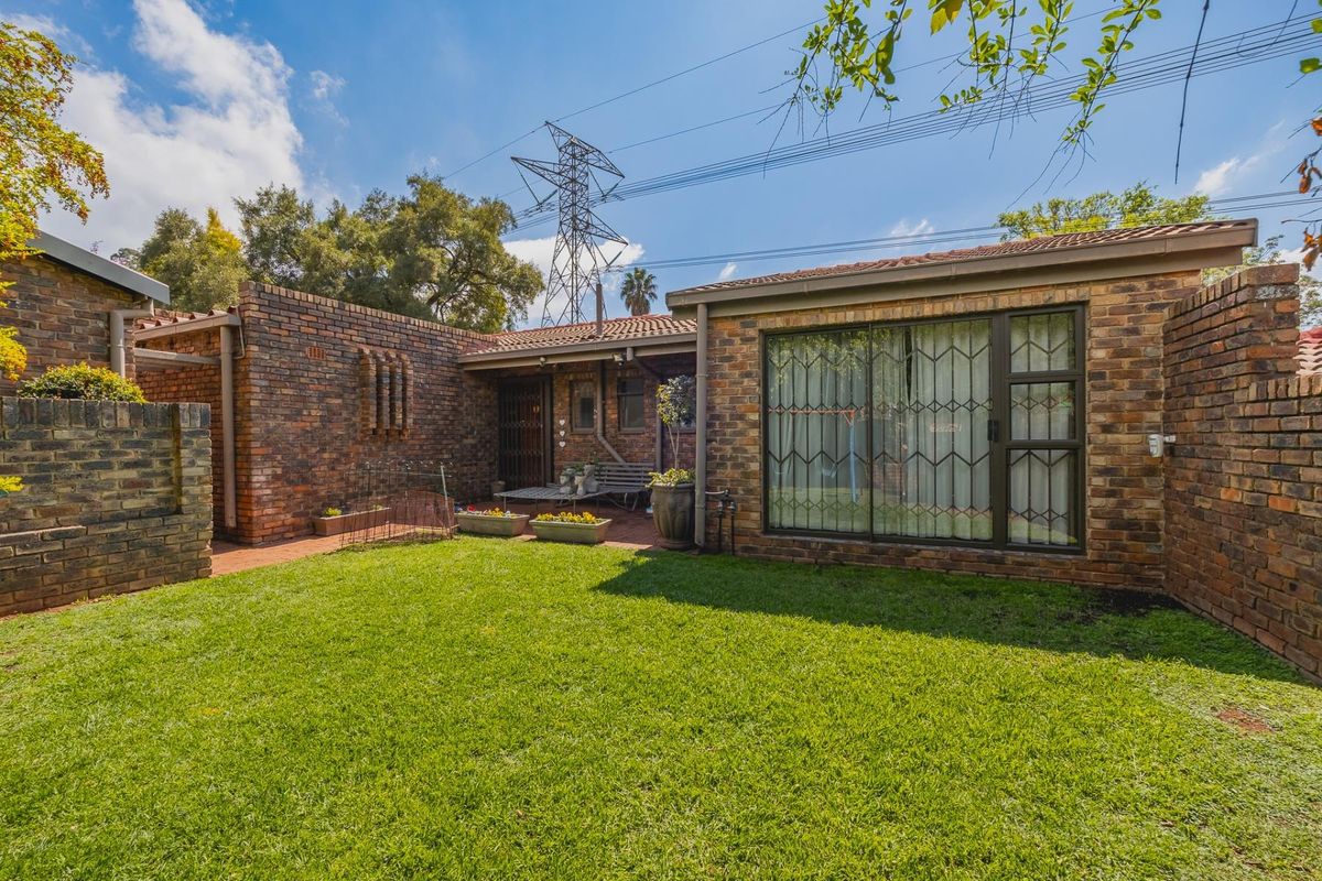 Rear view of the townhouse featuring a face brick facade, a paved patio area, and a well-maintained private lawn.
