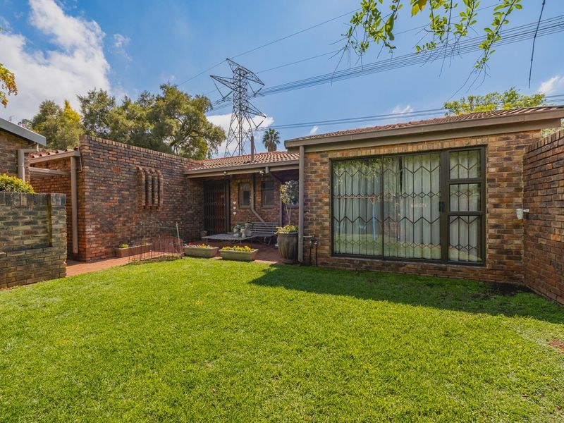 Rear view of the townhouse featuring a face brick facade, a paved patio area, and a well-maintained private lawn.