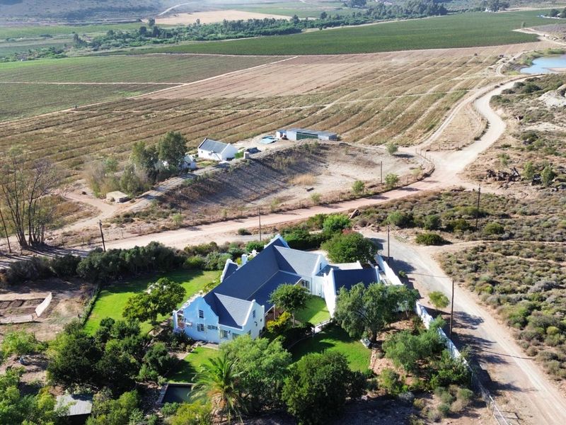 Aerial view of a rural property featuring a main residence with a pitched roof, swimming pool, and expansive surrounding farmland and natural landscape.