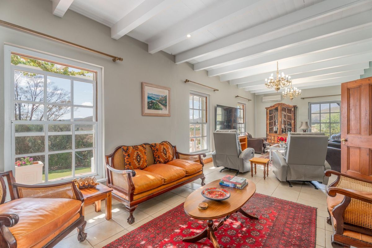 Spacious living room featuring exposed timber ceiling beams, tiled flooring, and large sash windows that provide ample natural light and scenic views.
