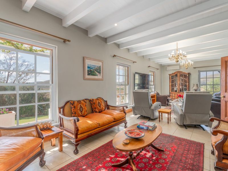 Spacious living room featuring exposed timber ceiling beams, tiled flooring, and large sash windows that provide ample natural light and scenic views.