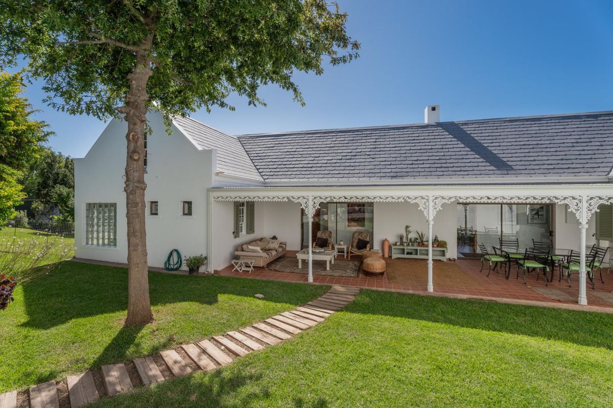 A well-maintained rear elevation featuring a spacious covered patio with decorative ironwork, terracotta flooring, and direct access to the garden through sliding doors.
