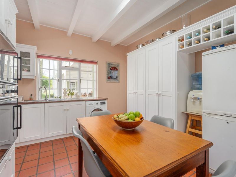 A functional kitchen featuring white cabinetry, built-in oven, exposed ceiling beams, and terracotta-style tiled flooring, offering a bright and practical workspace.