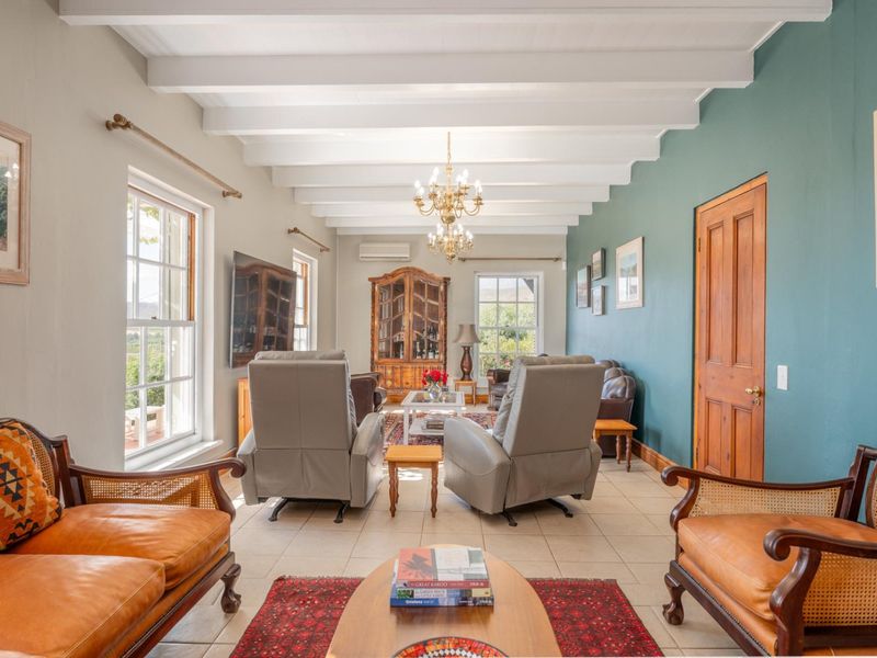 A well-maintained living room featuring exposed white timber beams, tiled flooring, sash windows, and a classic chandelier, creating a bright and inviting atmosphere.