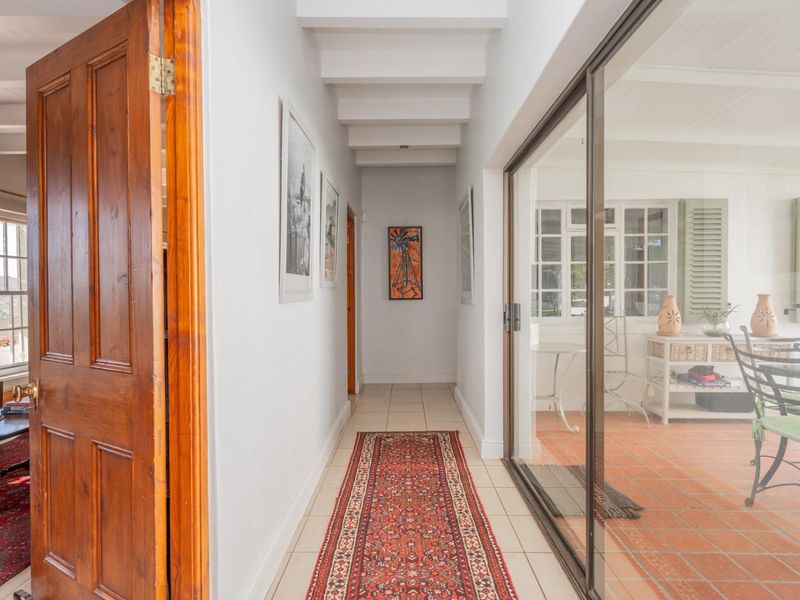 A bright hallway featuring exposed ceiling beams, tiled flooring, and large sliding glass doors that provide a view into the adjacent sunroom.