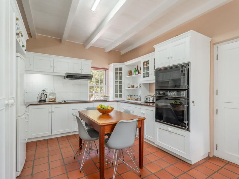 A well-maintained kitchen featuring white cabinetry, a double wall oven, exposed beam ceilings, and terracotta-style tiled flooring.