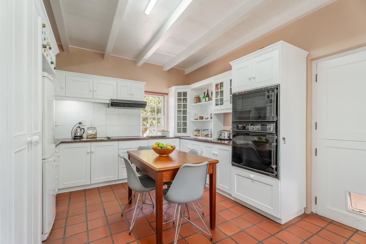 A well-maintained kitchen featuring white cabinetry, a double wall oven, exposed beam ceilings, and terracotta-style tiled flooring.