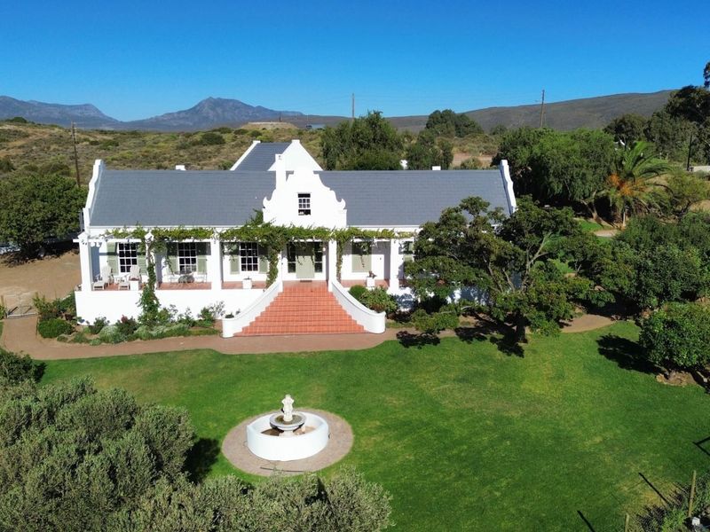 Aerial view of a classic Cape Dutch style house featuring a prominent gable, terracotta entrance stairs, covered veranda, and a well-maintained garden with fountain.