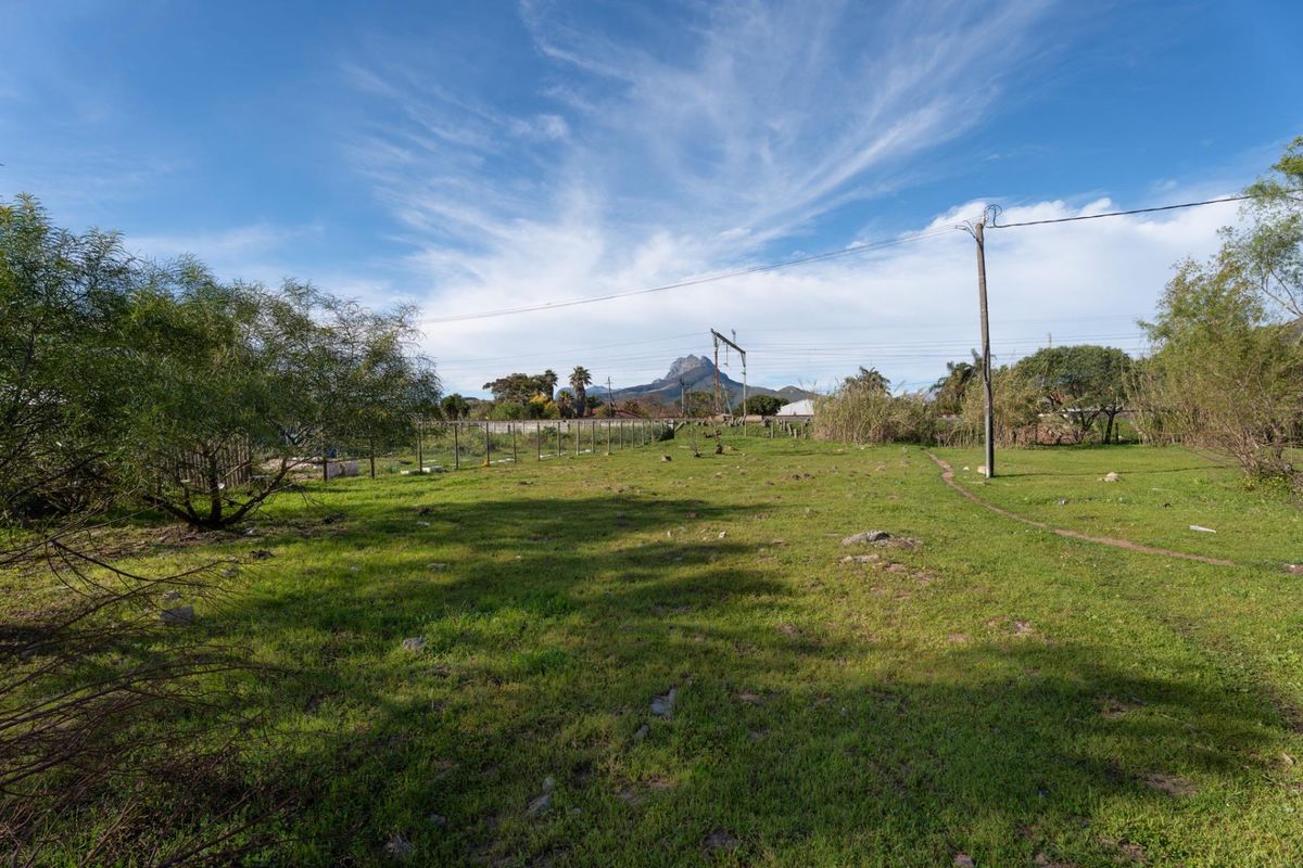 A vacant residential plot featuring grassy terrain, perimeter wire fencing, and utility infrastructure with mountain views in the background.