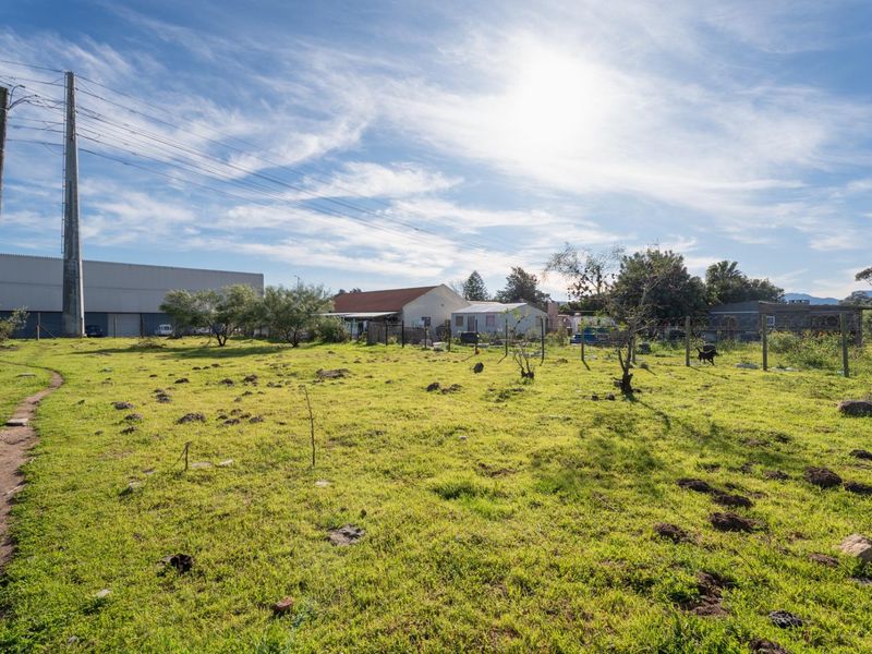 A view of a vacant residential plot featuring open grassland, perimeter wire fencing, and an adjacent utility pole.