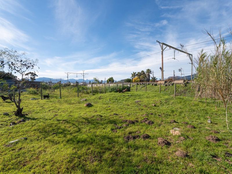 A view of a vacant residential plot featuring grassy terrain, perimeter wire fencing, and overhead utility infrastructure.