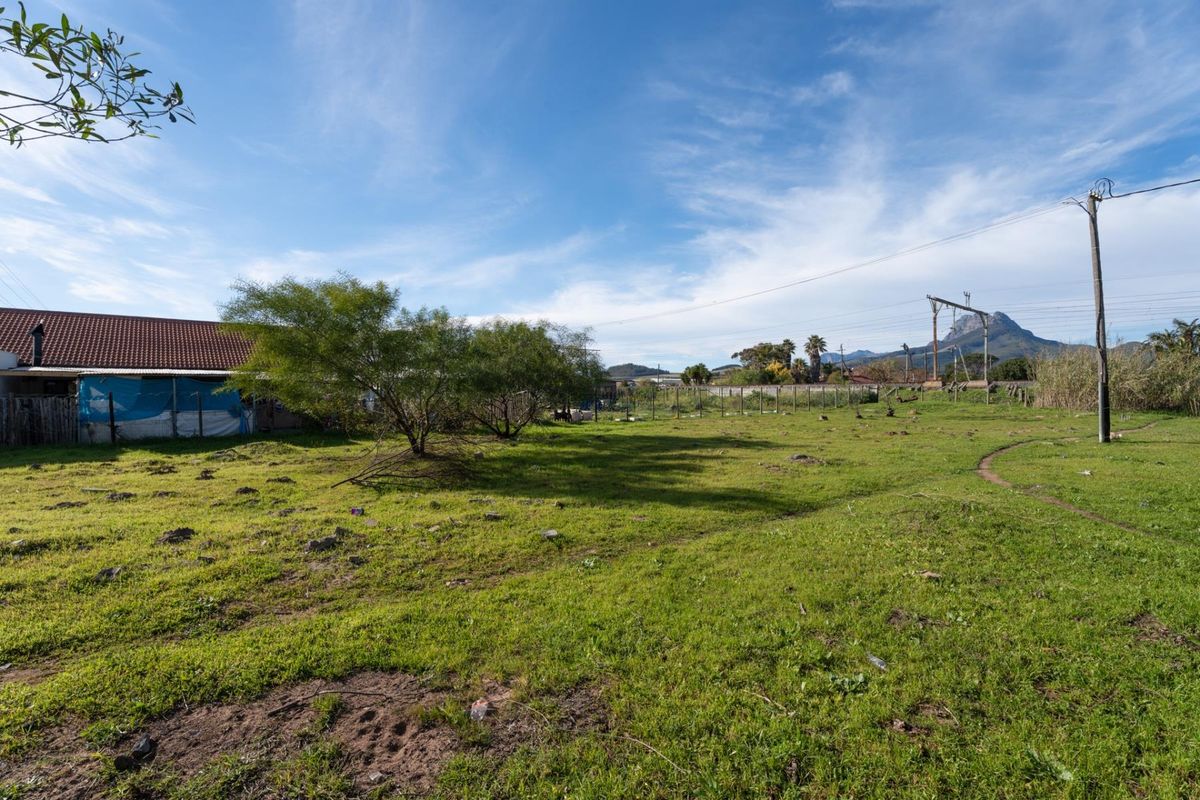 A view of a vacant residential plot featuring grassy terrain, perimeter wire fencing, and utility infrastructure with mountain views in the background.