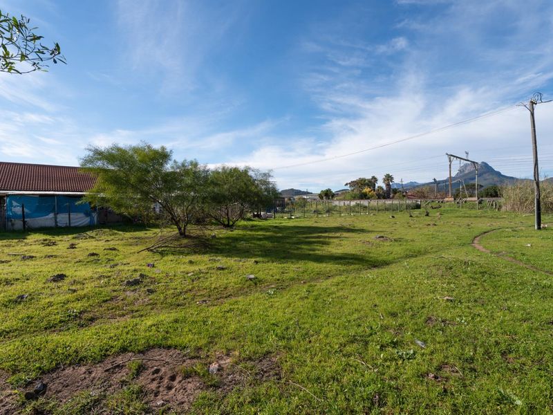 A view of a vacant residential plot featuring grassy terrain, perimeter wire fencing, and utility infrastructure with mountain views in the background.