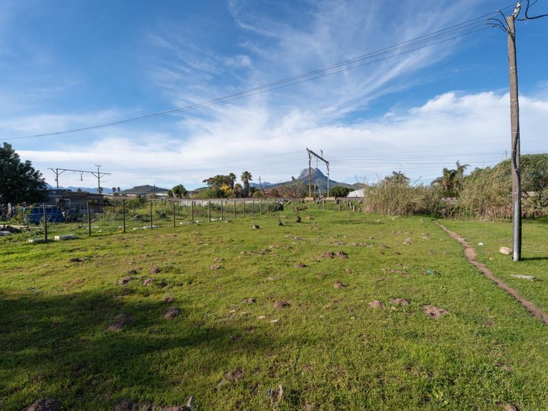 A view of a vacant residential plot featuring grassy terrain, perimeter wire fencing, and overhead utility infrastructure with mountain views in the distance.
